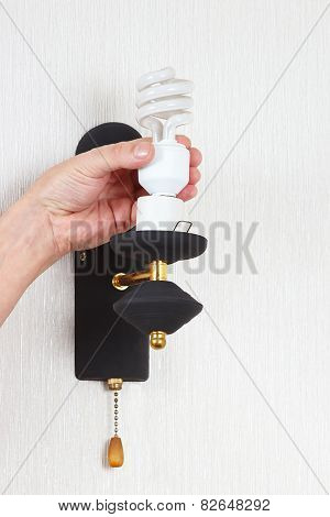 Hand unscrews tungsten bulb in luminaire on white wall