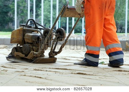 Worker in overalls controls plate compactor