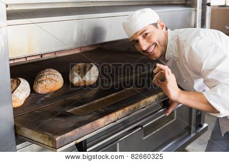 Happy baker by open oven in the kitchen of the bakery