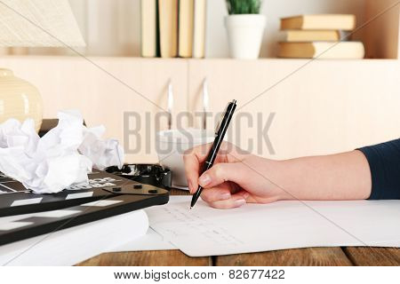 Female hand with pen at desktop with moving clapper and working mess on light cupboard background