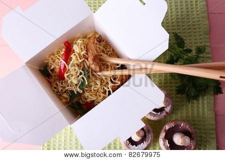 Chinese noodles and sticks in takeaway box on green napkin on pink background