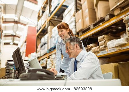 Warehouse managers working together on laptop in a large warehouse