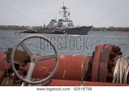 STATEN ISLAND, NY - MAY 20 2015: USS Barry (DDG 52) is guided into port by McAllister tugboats at Sullivans Pier, with red pipes in the foreground, at the beginning of Fleet Week.