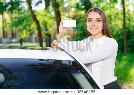 Pretty girl leaning on car and showing card