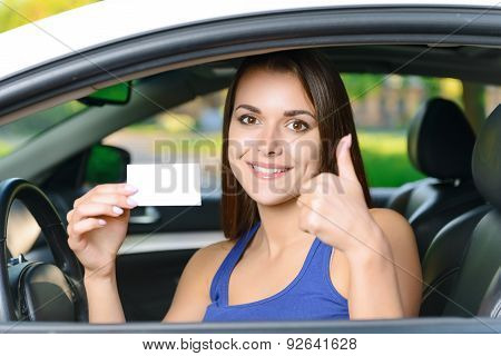 Attractive woman inside car showing card