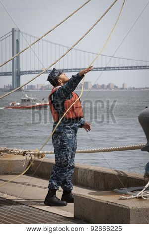 STATEN ISLAND, NY - MAY 20 2015: A sailor from NWS Earle Port Services tends the lines of the guided-missile destroyer USS Barry (DDG 52)  as the ship docks at Sullivans Pier for Fleet Week NY.