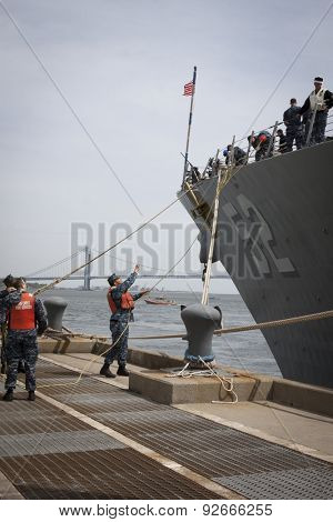 STATEN ISLAND, NY - MAY 20 2015:  A sailor from NWS Earle Port Services throws a line to personnel of guided-missile destroyer USS Barry (DDG 52) as the ship docks at Sullivans Pier for Fleet Week NY.