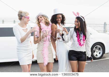 Frivolous women drinking champagne next to a limousine on a night out