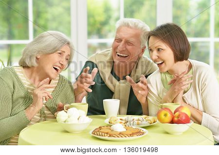 Cute family portrait , adult daughter with senior parents drinkig tea