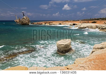 maritime landscape - boat shipwrecked near the rocky shore - turquoise sea with waves on background of cloudy sky. Cliffs in water. The Mediterranean coast near Paphos Cyprus