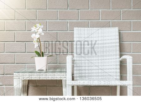 Closeup artificial plant with white orchid flower on pink flower pot on wood weave table with wood weave chair on blurred brown brick wall texture background beautiful interior in relaxation concept