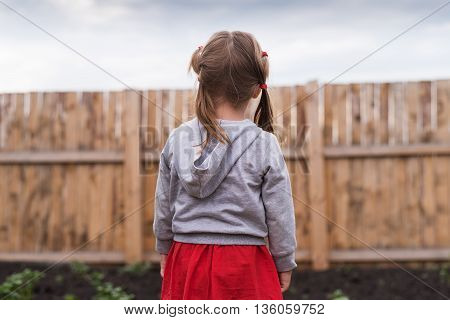 Little girl standing in front of a wooden fence in the garden on a summerday.