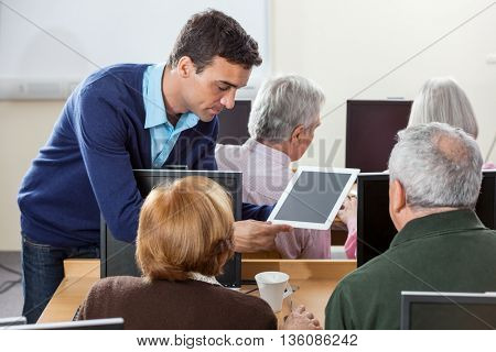 Teacher Showing Digital Tablet To Senior Students In Computer Cl