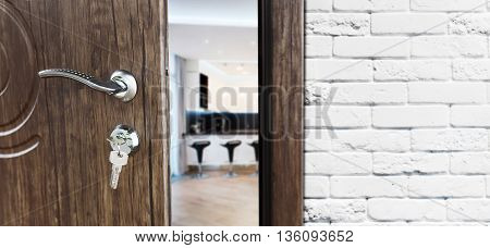 Half opened door to a kitchen. Door handle, door lock. Dining room door half open. Opening door. Welcome concept. Entrance to the room. Door at white brick wall, modern interior design.