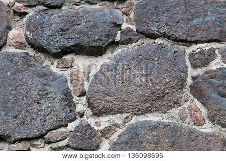 Wall of the medieval fortress of large stones. The texture is very old stone walls of the fortress. Background of cobblestones. The ancient construction of buildings from natural stones.