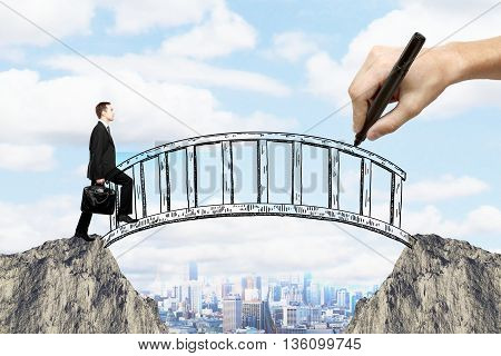 Success concept with hand drawing bridge over gap between two cliffs and businessman walking across it on city background