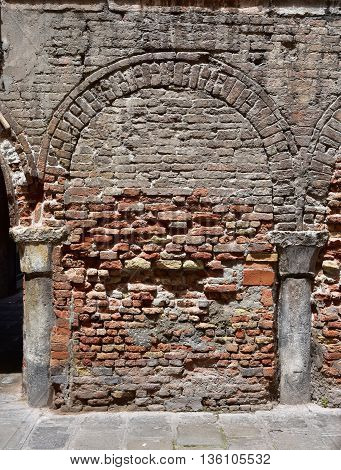 Brick wall with closed arch and columns buried in the old street level of Venice