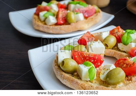 Italian starter friselle. Classical frisella tomato cheese mozzarella olives and basil with oregano and olive oil. Dried bread called freselle on white plate. Italian food. Healthy vegetarian food.