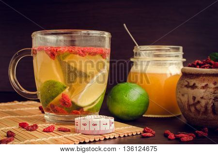 Cup of delicious dietary Goji berry tea with lime and honey on wooden background with measuring tape. Wolfberry for a healthy diet. Alternative medicine. Recovery. Rejuvenation. Slimming.