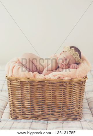 Adorable little guy with little fluffy hairs,in a beige knitted crown,sound asleep on the soft beige blanket in a large wicker basket high,sweet sleeping newborn baby