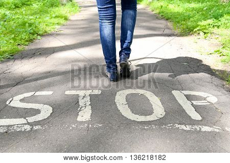 Stop sign painted on the road and female legs next to the sign.