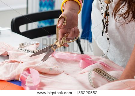 Close up view of female dress maker hands cutting something. Dressmaker works at her atelier. Handmade clothes