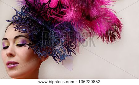 Close-up portrait of beautiful young woman in lace lilac purple hat fascinator with feathers on white background. Fashion professional violet purple shades make-up. Model shot.