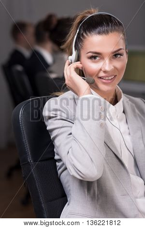 Young female telephone consultant sitting on a chair and listening to a client voice in headphones