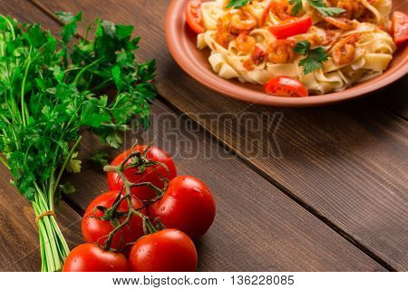 Fettuccine pasta with shrimp tomatoes and herbs. wooden background
