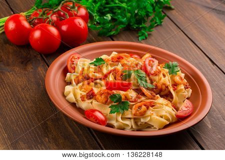 Fettuccine pasta with shrimp tomatoes and herbs. wooden background