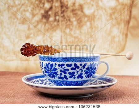 Blue pattern painted vintage cup of tea with brown sugar stirrer on top