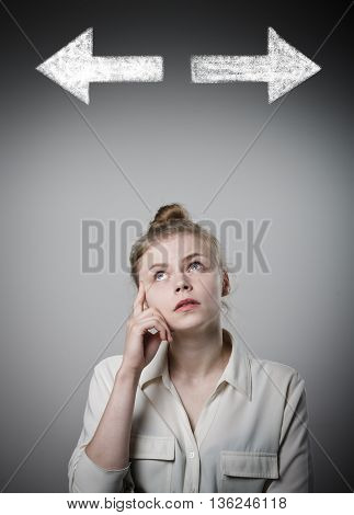Young slim woman has to decide between two directions. Girl in white full of doubts and hesitation.