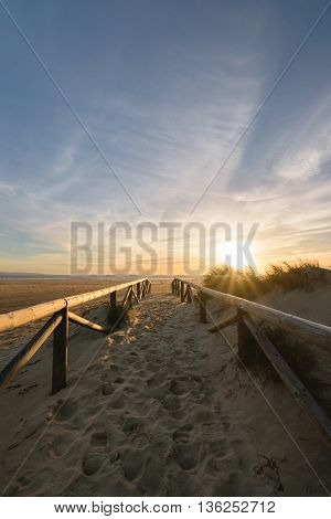 A path on the sand going to the Atlantic Ocean in Tarifa, Spain. The photo is taken during an amzing colorful sunset with golden light.