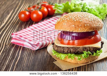 Homemade cheeseburger with beef patties and fresh salad on seasame buns, sered on brown wooden table.