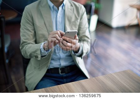 Handsome man working with smartphone and documents at cafe
