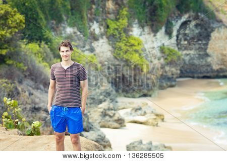 Young handsome man is standing on the rock under the beach