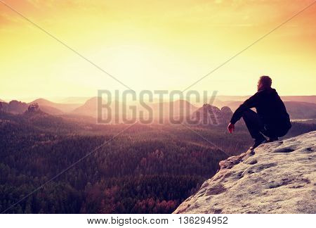 Adult In Black Trousers, Jacket Sit On Cliff's Edge