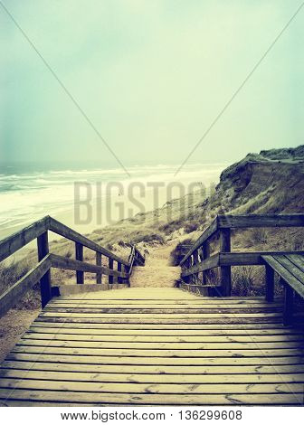 Lonely footpath or wooden stairway through a beach dune. Beach on Sylt with stormy sky