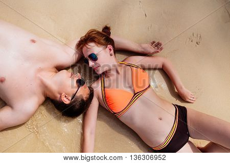 Young couple lying on the beach near the water, facing each other, the morning sun tan