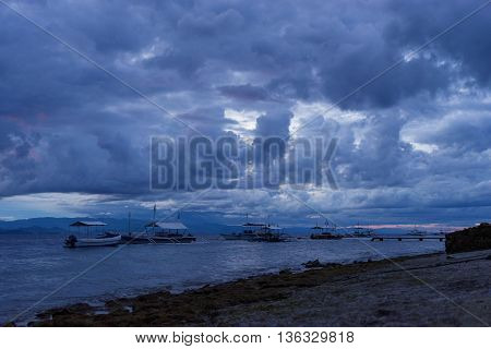 stormy dark sunset in tropical sea with fishing and diving wooden boat near stone coastline and