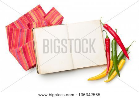 Old cookbook and different colors chilli peppers isolated on white background.