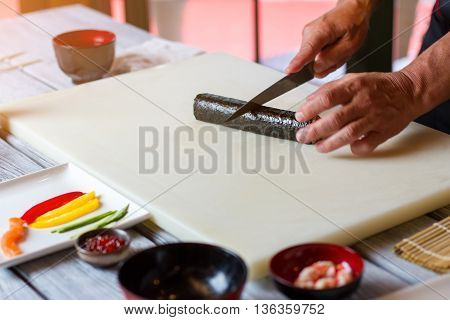Hand with knife cuts sushi. Long sushi roll. Japanese chef cooks futomaki rolls. Kitchen table in sushi restaurant.
