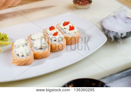 Sushi with caviar on plate. Cooking board with sushi plate. Uramaki rolls and dry ice. Sushi cafe at daytime.