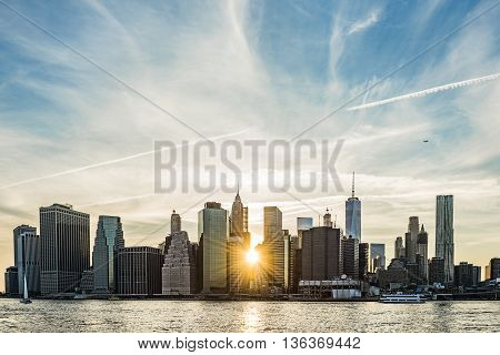 Sunburst between buildings of the Manhattan skyline in New York City during sunset with airplane