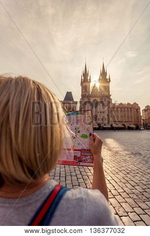 Young girl in Prague looks at the city map in the old town square. Travel guide, tourism in Europe, woman tourist with map on the street. Kostel Panny Marie pred Tynem. Church of the Virgin Mary.