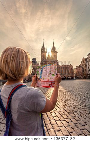 Young girl in Prague looks at the city map in the old town square. Travel guide, tourism in Europe, woman tourist with map on the street. Kostel Panny Marie pred Tynem. Church of the Virgin Mary.