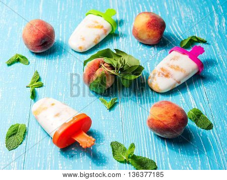 Homemade popsicles with peach and mint on blue wooden table closeup