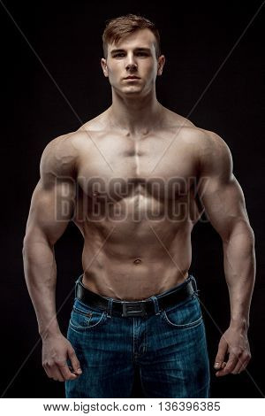 Muscular bodybuilder guy doing posing over black background. Naked torso in jeans. He looks into the camera