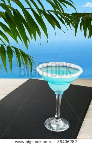 Blue cocktail on the tropical beach. Blue Lagoon margarita martini cocktail. Summer beach alcohol drink. Iced blue cosmopolitan cocktail.