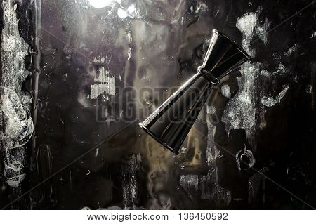 Shiny stainless steel jigger for alcoholic beverage on a solid ice